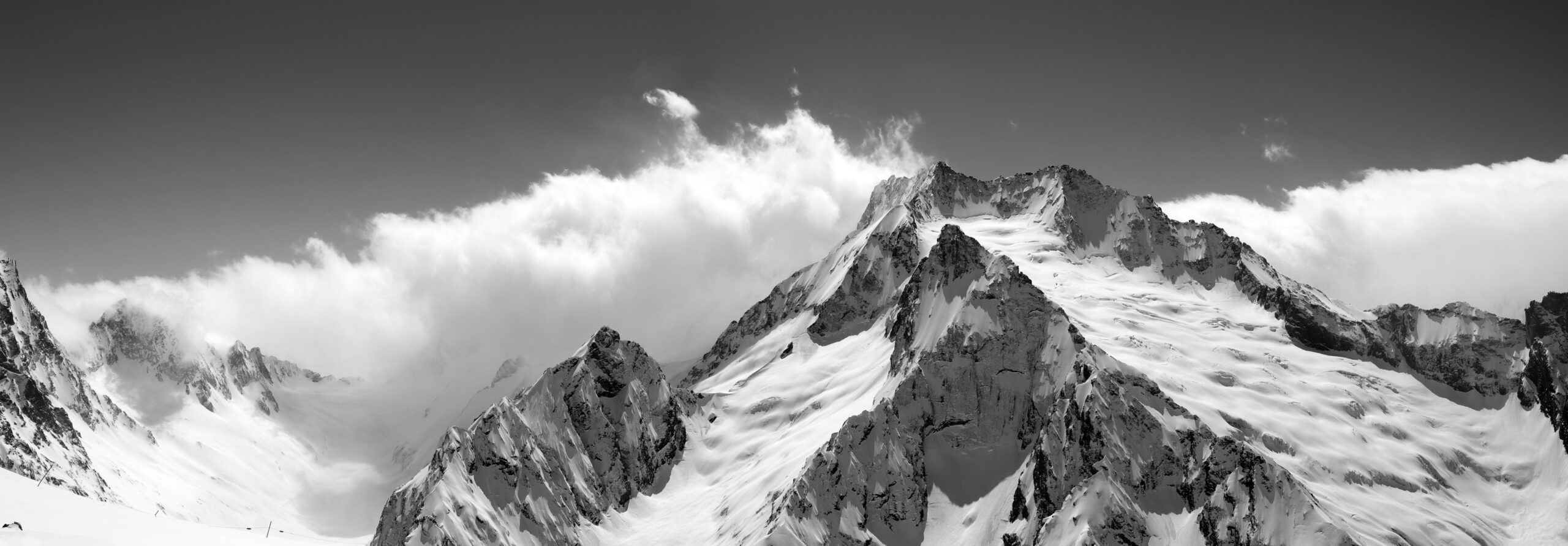 Schwarzweißaufnahme von schneebedeckten Berggipfeln vor Wolken